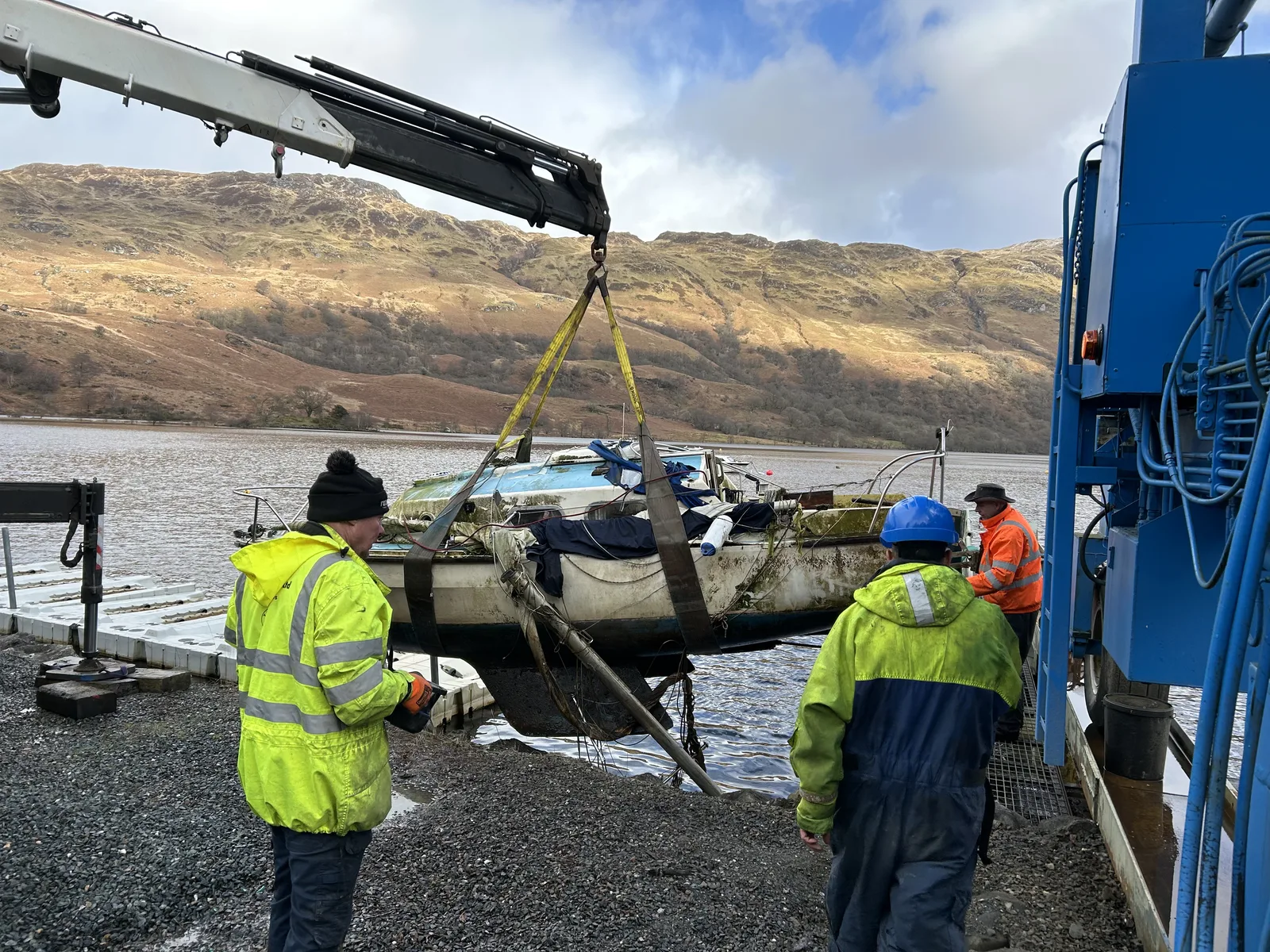 Boat being lifted from the water with workers standing nearby