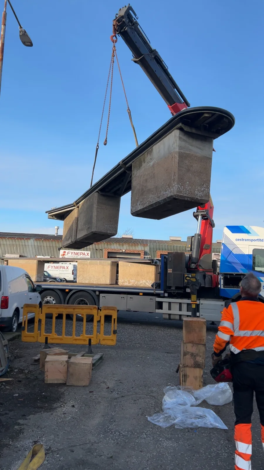 Lorry-mounted crane lifting concrete sections near a waterside work area